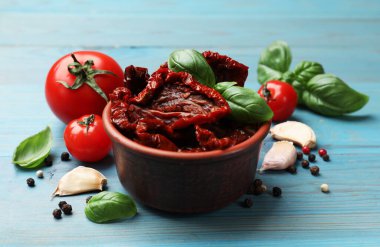 Lezzetli güneş kurutulmuş domatesler kasede, taze sebzeler ve baharatlar açık mavi ahşap masada, yakın plan.