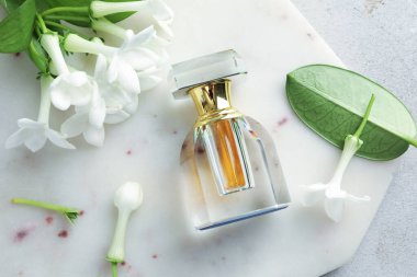 Parfüm ve yasemin çiçekleri açık gri masada, üst tarafta.