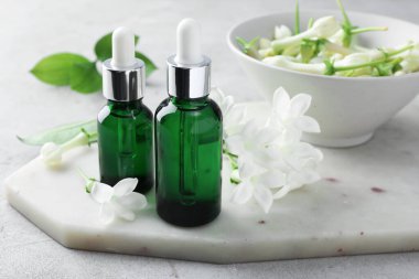 Açık gri masada yağlı şişeler ve yasemin çiçekleri, yakın plan.