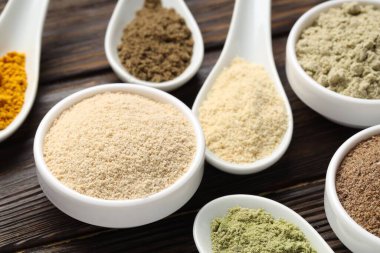 Tahta masadaki kaşıklarda ve kaselerde farklı süper yiyecek tozları, yakın plan.