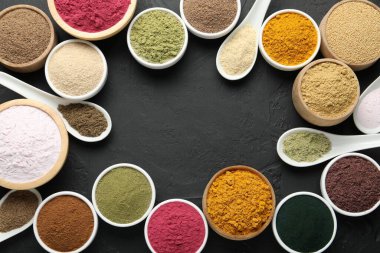 Kâselerdeki farklı süper yiyecek tozlarının çerçevesi ve koyu dokulu masa üzerindeki kaşıklar düz uzanıyordu. Metin için boşluk