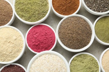 Gri desenli masada, düz yerde, kaselerde farklı süper yiyecek tozları var.