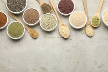 Farklı süper yiyecek tozları, gri desenli masa üzerinde kaşık ve kâseler halinde düz uzanıyordu. Metin için boşluk