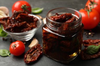 Lezzetli güneşte kurutulmuş domatesler ve taze sebzeler siyah masada, yakın plan.