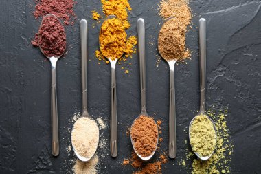 Siyah masanın üzerinde kaşıklarda farklı süper yiyecek tozları var.