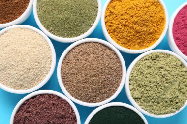 Açık mavi arka planda, kaselerde farklı süper yiyecek tozları var.