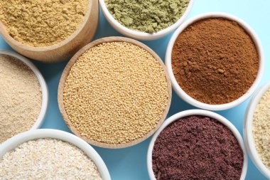 Açık mavi arka planda, kaselerde farklı süper yiyecek tozları var.