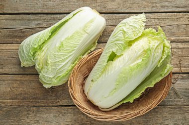 Hasır sepetin içinde taze Çin lahanaları, ahşap masa, üst manzara.