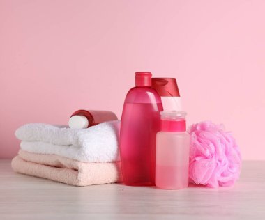 Açık ahşap masada pembe arka planda farklı banyo aksesuarları.