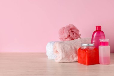 Pembe arka planda açık ahşap masada farklı banyo aksesuarları. Metin için boşluk