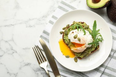 Avokadolu lezzetli sandviç, haşlanmış yumurta, roka ve balkabağı beyaz mermer masada servis ediliyor. Metin için boşluk