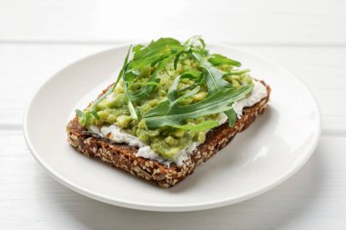 Avokado, krem peynir ve roka ile nefis sandviç beyaz ahşap masada, yakın plan.