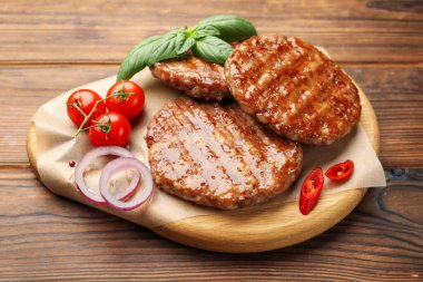 Lezzetli hamburger köfteleri, domatesler ve baharatlar ahşap masada, yakın plan.