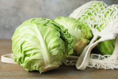 Taze lahanalar ve ahşap masada ağ torba, yakın plan.