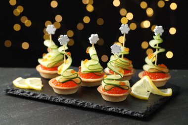 Siyah masadaki lezzetli kanepeler karanlık arka planda bulanık ışıklarla, yakın plan. Bokeh etkisi