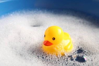 Mavi arka planda köpüklerle suda yüzen sevimli plastik ördek, yakın plan.