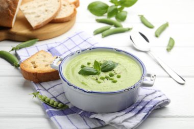 Beyaz ahşap masada fesleğenli bezelye kremalı çorba.
