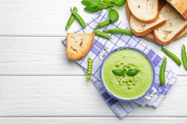 Beyaz ahşap masada servis edilen fesleğenli bezelye kremalı çorba. Metin için boşluk