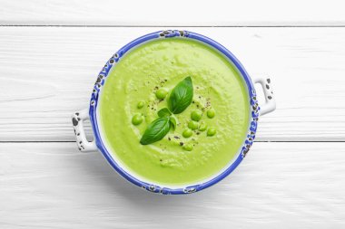 Beyaz ahşap masada fesleğenli bezelye kremalı çorba.