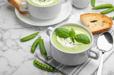 Fesleğenli bezelye kremalı çorba beyaz mermer masada servis edilir.