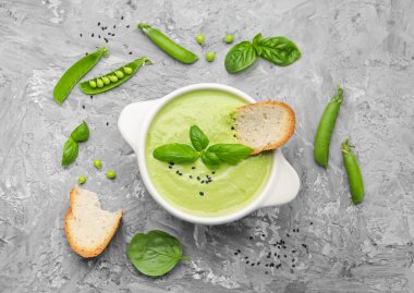 Lezzetli bezelye kremalı çorba fesleğen ve kızarmış ekmek gri masada servis edilir.