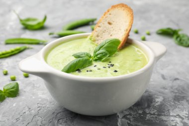 Lezzetli bezelye kremalı çorba fesleğen ve kızarmış ekmek, yakın plan, gri masada servis edilir.