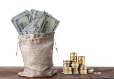 Zenginlik. Bir çuval dolusu para ve bozuk paralar beyaz arka plana karşı ahşap masaya istiflenmiş.