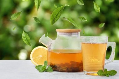 Yeşil çay yaprakları açık havada beyaz masada sıcak içecek üzerinde uçuyor.