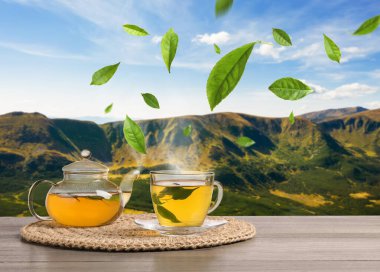 Yeşil çay yaprakları sıcak içeceğin üzerinde uçuyor dağlardaki ahşap masada.