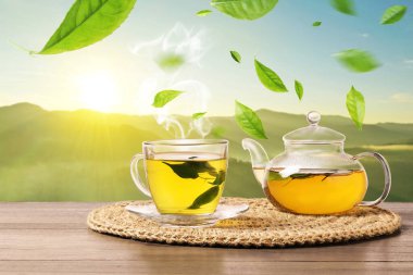 Yeşil çay yaprakları sıcak içeceğin üzerinde uçuyor dağlardaki ahşap masada.