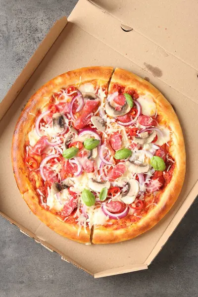 Tütsülenmiş sosis ve karton kutuda mantarlı lezzetli pizza. Gri desenli masa, üst manzara.