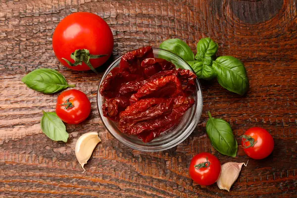 Lezzetli güneş, cam kasede kurutulmuş domatesler, taze sebzeler ve ahşap masada baharatlar, düz uzanmış.