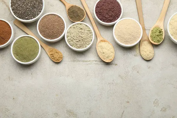 Farklı süper yiyecek tozları, gri desenli masa üzerinde kaşık ve kâseler halinde düz uzanıyordu. Metin için boşluk