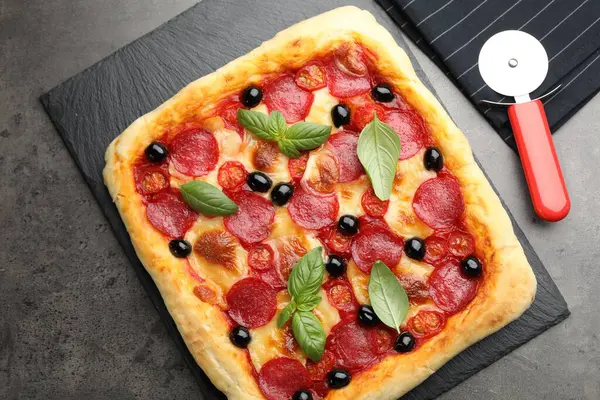 Lezzetli ev yapımı pizza ve kesme makinesi gri masada, üst tarafta.