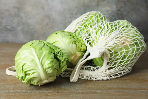 Taze lahanalar ve ahşap masada ağ torba, yakın plan.