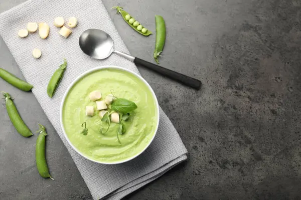 Lezzetli bezelye kremalı çorba, kızarmış ekmek, fesleğen ve mikroyeşillikler gri masada servis edilir. Metin için boşluk