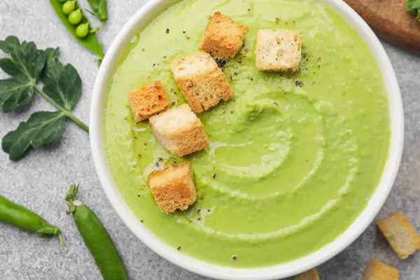 Gri masada servis edilen kıtır ekmekli bezelye kremalı çorba.