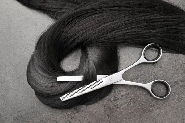 Gri yüzeyde siyah saç teli ve profesyonel makas, üst görünüm