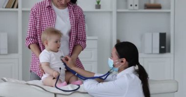 Annesi ve sevimli bebeğinin klinikteki çocuk doktoruyla randevusu var. Steteskopla çocuğu muayene eden doktor.