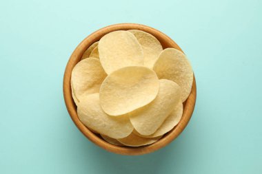 Açık mavi arka planda kasede patates cipsi, üst manzara.