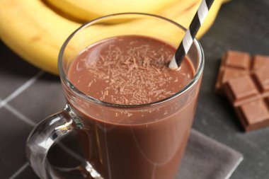 Cam bardakta lezzetli çikolatalı süt, siyah masada parçalar ve muzlar, yakın plan.