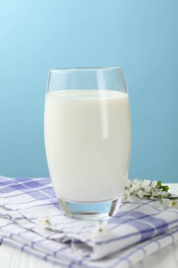 Bardaktaki taze süt ve beyaz ahşap masadaki çiçekler açık mavi arka planda, yakın plan.