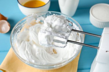 Açık mavi masada çırpılmış krema ve çırpılmış çırpılmış çırpılmış çırpıcı, yakın plan.