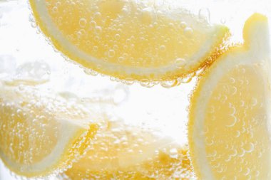 Beyaz arka planda limon dilimleri ile soda tazeleniyor, yakın plan.