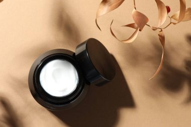 Bej arka planda bir kavanoz vücut kremi ve kuru dallar, üst manzara.