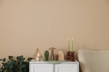 Havalı şamdanlar, yanan mumlar ve kapalı alandaki bej duvarın yanındaki dolaptaki diğer dekorlar.