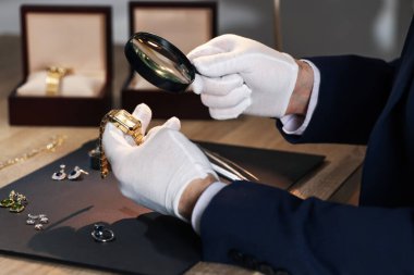 Büyüteci olan bir eksper. Masadaki lüks kol saatini değerlendiriyor. Yakın plan.