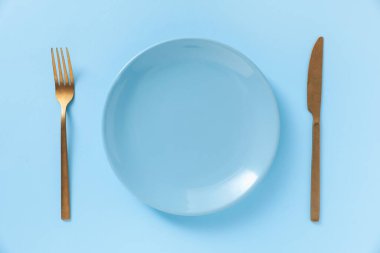 Açık mavi zemin üzerinde şık tabak ve çatal bıçak takımı, düz.