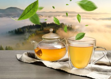 Yeşil çay yaprakları sıcak içeceğin üzerinde uçuyor dağlardaki ahşap masada.