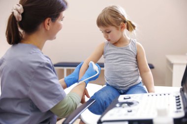 Sonograf klinikte küçük bir kızın kolunun ultrason muayenesini yapıyor.